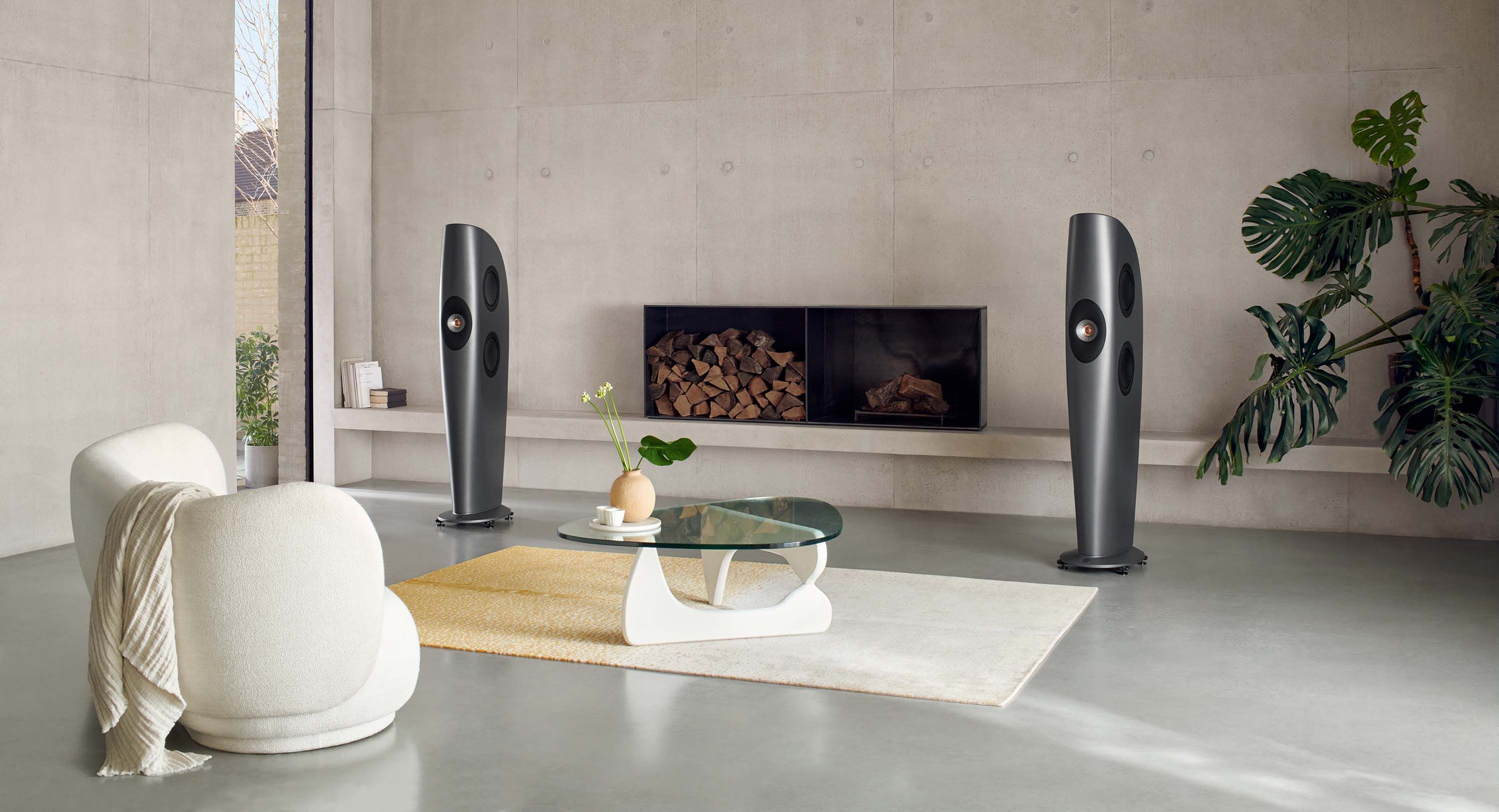A pair of Kef Blade series speakers in a large minimalist room with concrete floors and walls